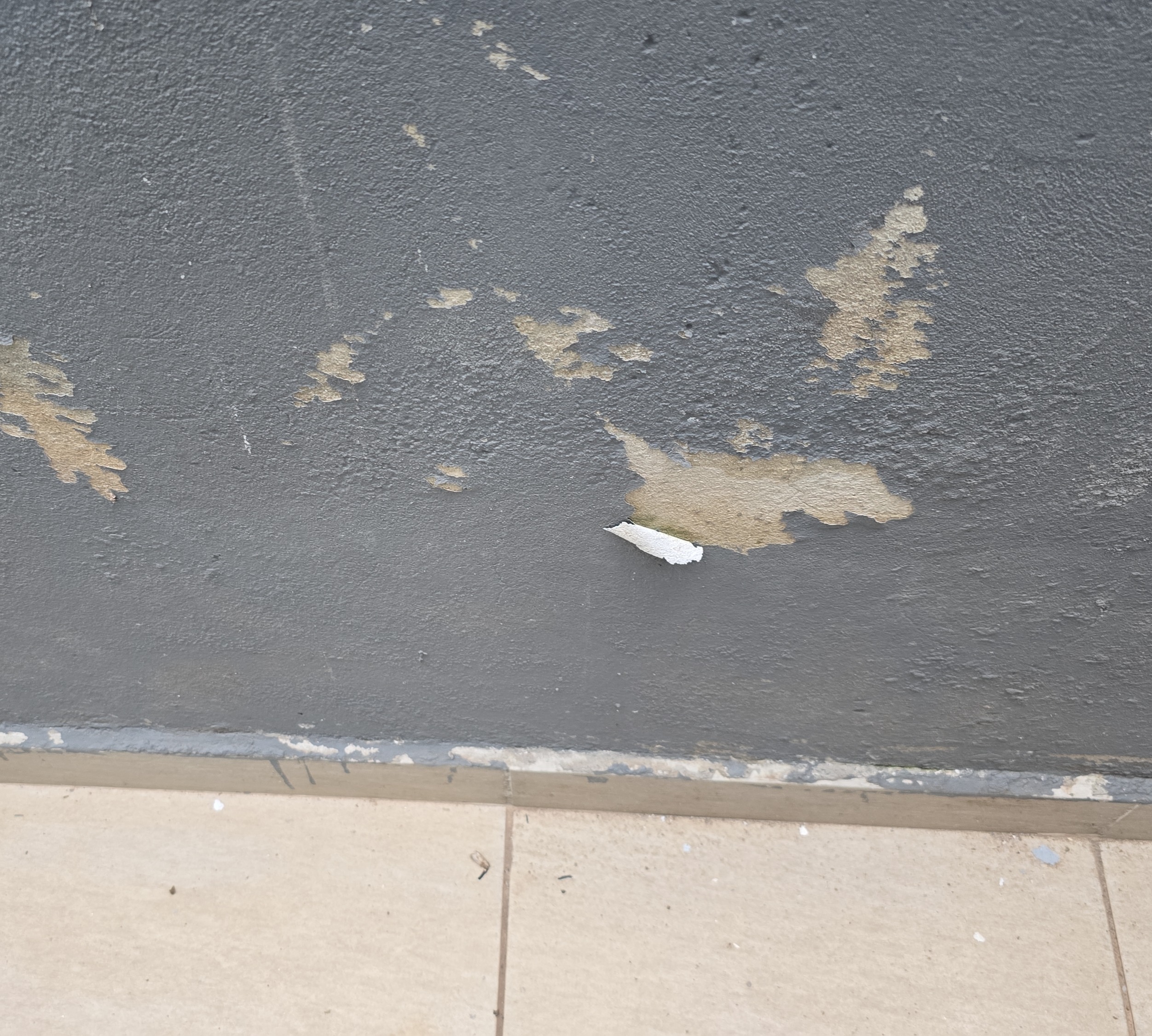 Descascamento de pintura em parede com revestimento texturizado, indicando perda de aderência e degradação superficial.