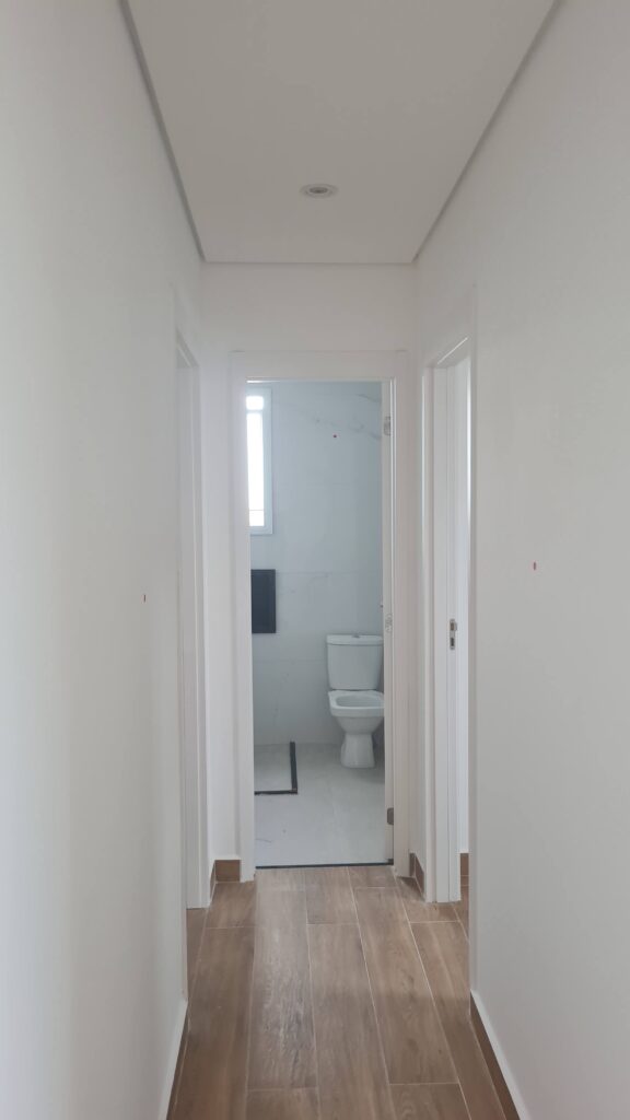 Corredor interno com piso cerâmico amadeirado durante vistoria de apartamento novo.