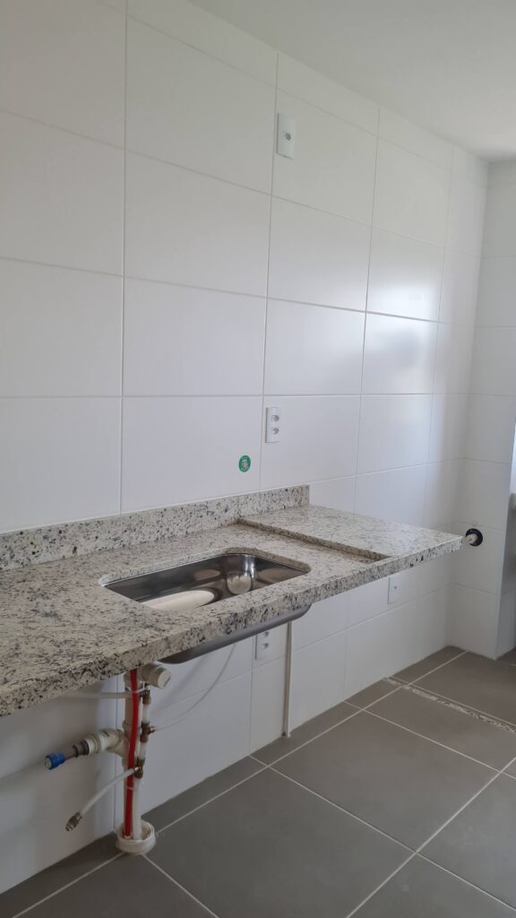 Área de serviço de imóvel novo com bancada em granito, tanque, revestimento cerâmico e pontos hidráulicos avaliados durante vistoria técnica.