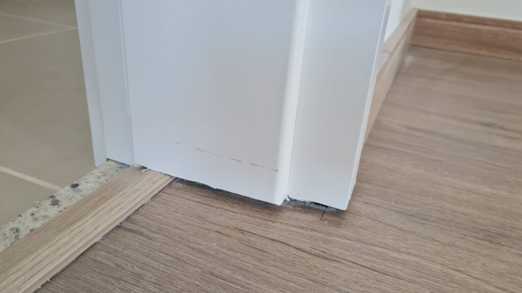 Detalhe de guarnição de porta, rodapé e piso amadeirado de imóvel novo durante vistoria técnica de acabamento.