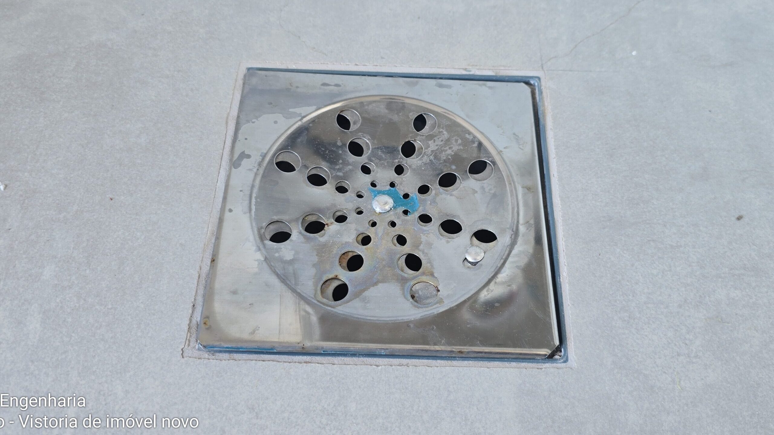 Ralo de piso em área de serviço com encaixe solto identificado durante vistoria técnica de imóvel novo.